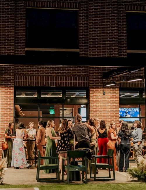 An outdoor party in a brick courtyard with guests mingling, tables set up, and string lights glowing at night.