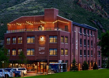 It's an image of a brick building with a lit rooftop, surrounded by hills. Cars are parked in front, and there are lights strung above.