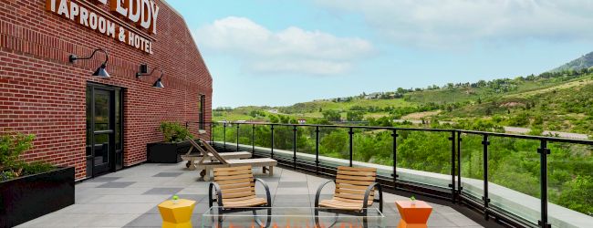 Outdoor seating area with fire pit at "The Eddy Taproom & Hotel," featuring chairs and tables on a terrace with a scenic view.